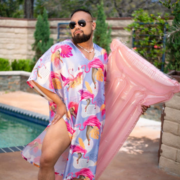 Bearded man in sunglasses wearing the Flamingle caftan poolside, holding a pink pool float