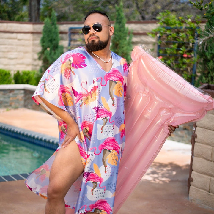 Bearded man in sunglasses wearing the Flamingle caftan poolside, holding a pink pool float